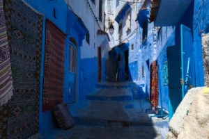 Narrow blue alleyway with carpets hanging on walls.