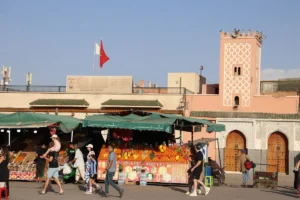 People at a market with fruit stalls and pink building.