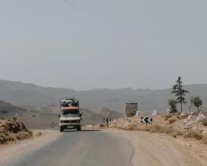 Truck driving on a dusty desert road with mountains.