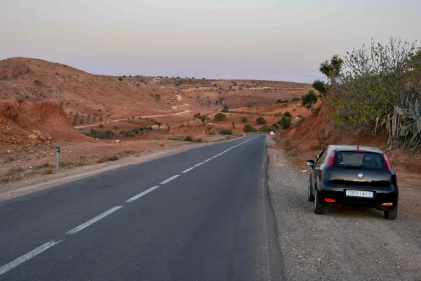 A narrow asphalt road winding through the sandy desert landscape of Morocco on a hot sunny summer day, a clear blue sky.