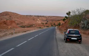 A narrow asphalt road winding through the sandy desert landscape of Morocco on a hot sunny summer day, a clear blue sky.