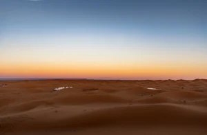 Desert sand dunes under a gradient sky at sunset